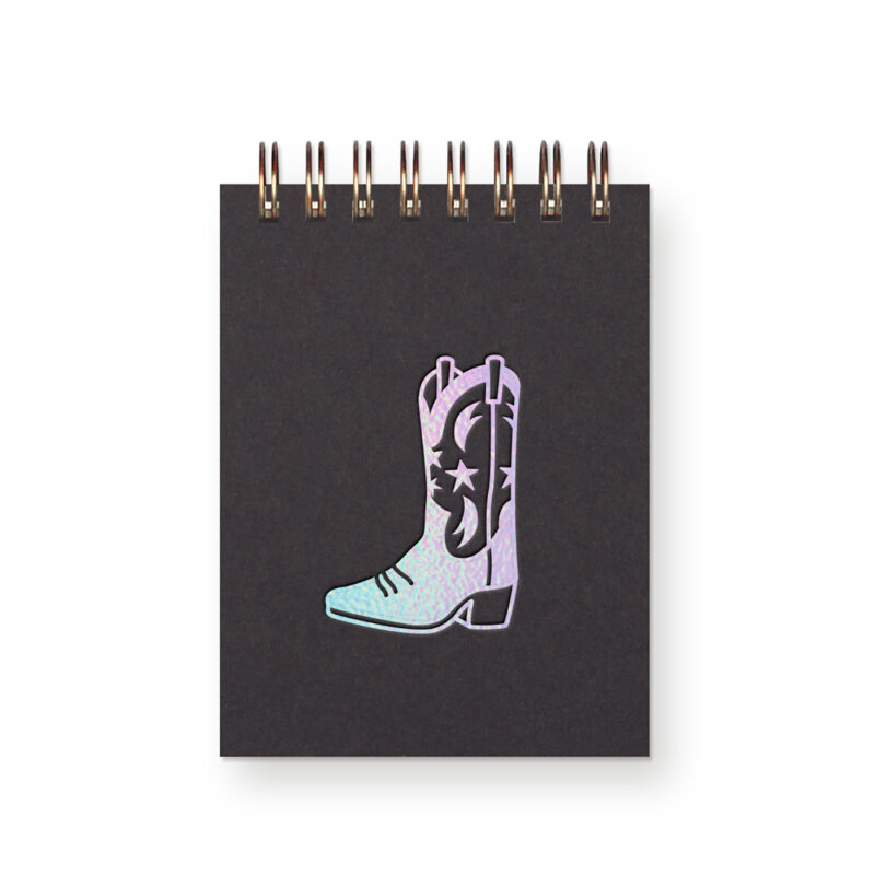 An iridescent foil cowboy boot on a black miniature notebook