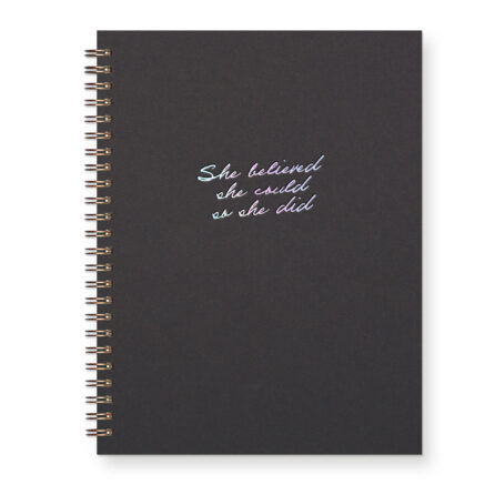 A script font reads "She believed she could so she did" in iridescent foil on a black journal
