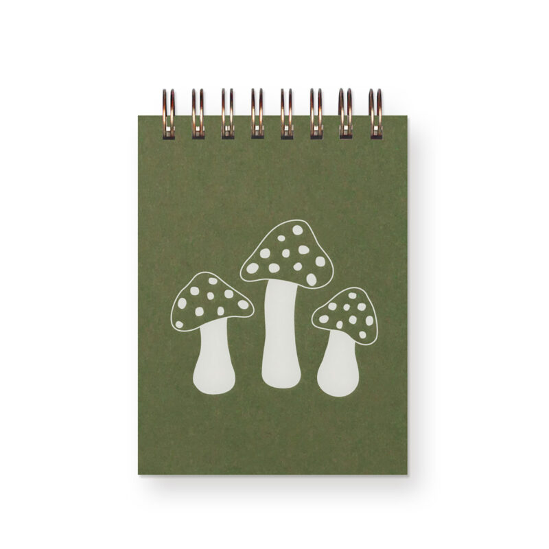 a miniature green notebook with three white toadstool mushrooms on it. It is spiral bound across the top.